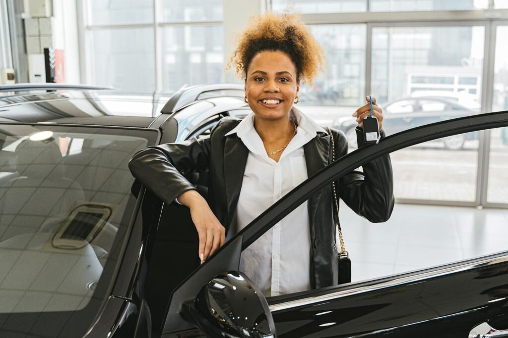 Contacto Tomas Cases Aspe Smiling woman with car keys standing beside her new vehicle in a dealership showroom.